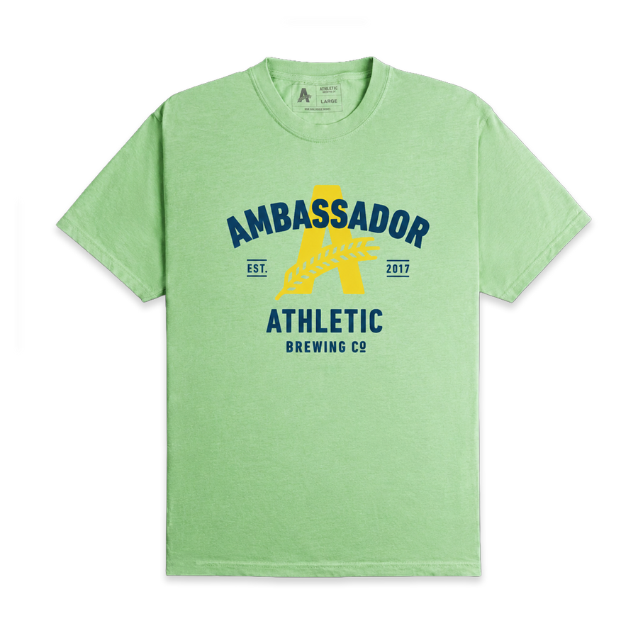 Light green Athletic Brewing Ambassador T-shirt featuring a large yellow “A” logo with a wheat graphic and navy text reading “AMBASSADOR,” “ATHLETIC BREWING CO,” and “EST. 2017” on the front chest.