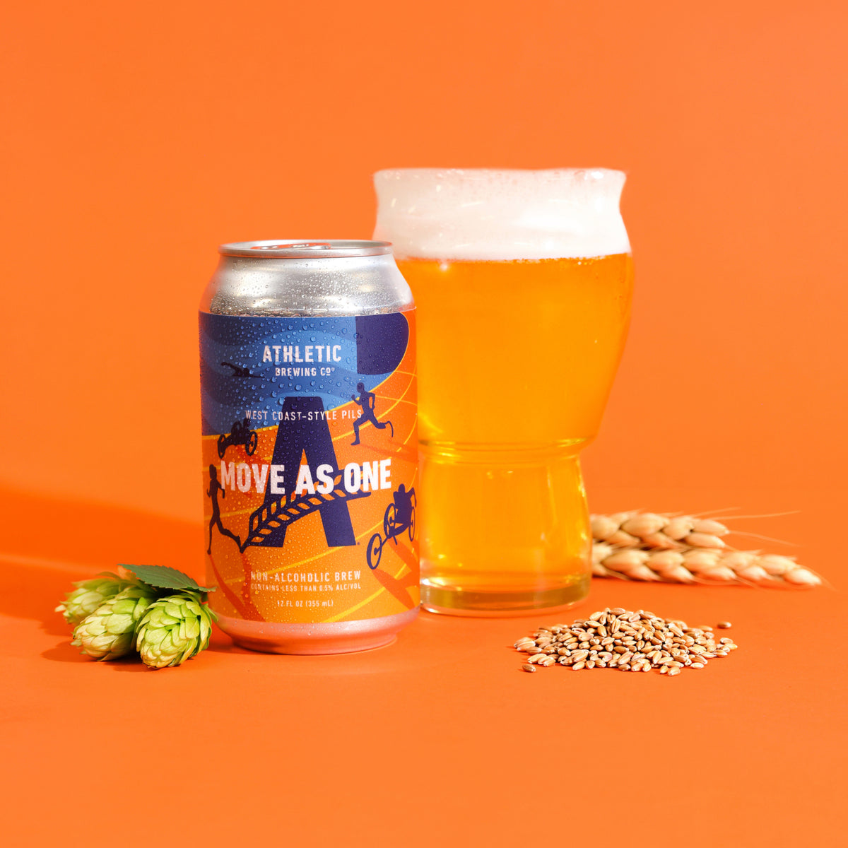 Athletic Brewing Move As One West Coast-Style Pils non-alcoholic beer can beside a glass of golden beer with a foamy head, surrounded by hops and grains against a vibrant orange background.